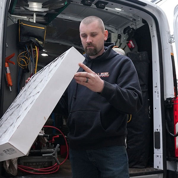 HVAC technician holding a box of air filters in front of the open backdoor of his work van.