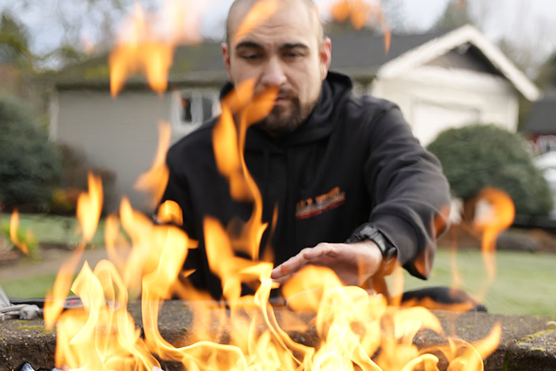 Fireplace technician sitting behind a lit outdoor gas fireplace.