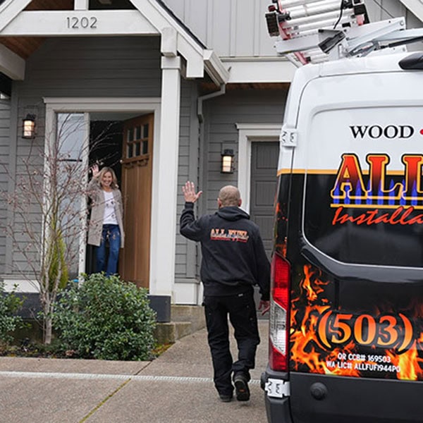 HVAC technician in a homes driveway waving at a homeowner standing in her doorway.