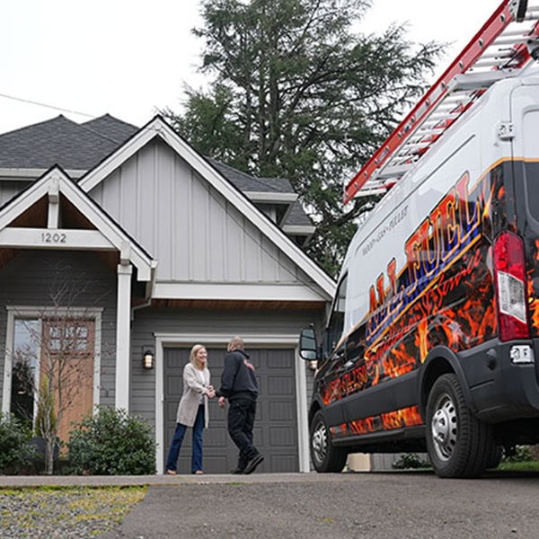 HVAC technician and homeowner shaking hands in the driveway of a home.
