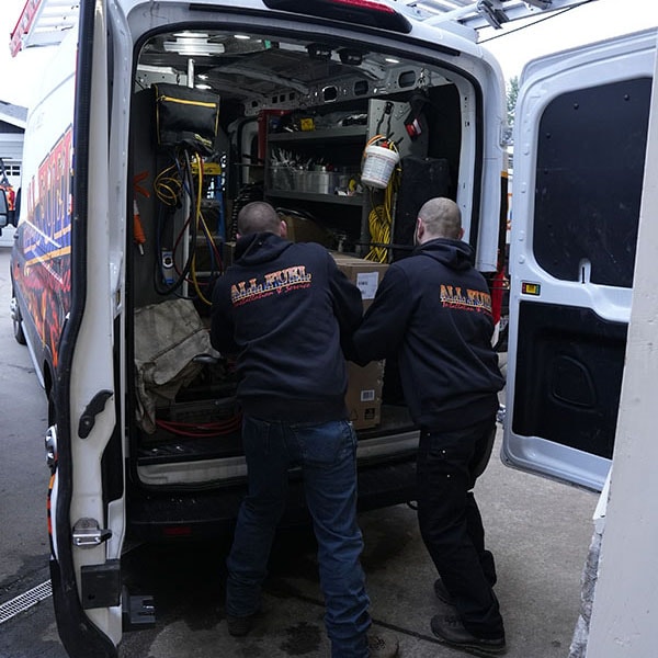 Two HVAC technicians pulling equipment out of their work van.