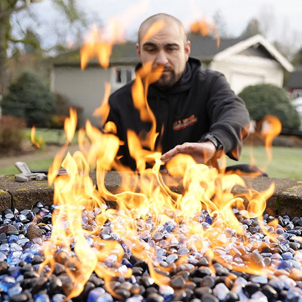 A gas fireplace with flames with a technician sitting behind it.