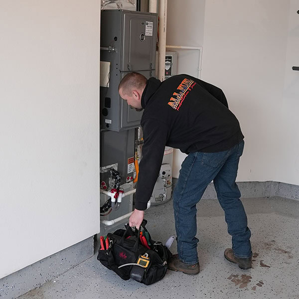 HVAC technician grabbing his tool bag next to a furnace in a homes garage.