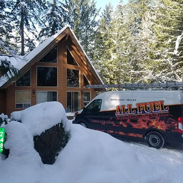 All Fuel work van parked in a snowy driveway of a cabin home.