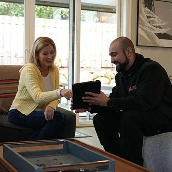 HVAC technician and homeowner sitting in the living room of a home showing her something on his company iPad.